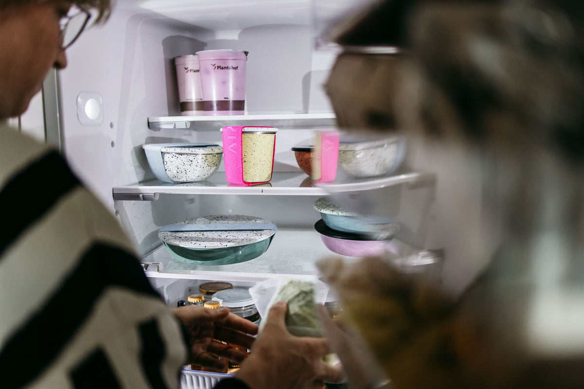 Zwei Personen schauen in einen Kühlschrank voller YIV Emaille Schalen mit Deckel – Reste schön aufbewahrt, kein Food Waste.